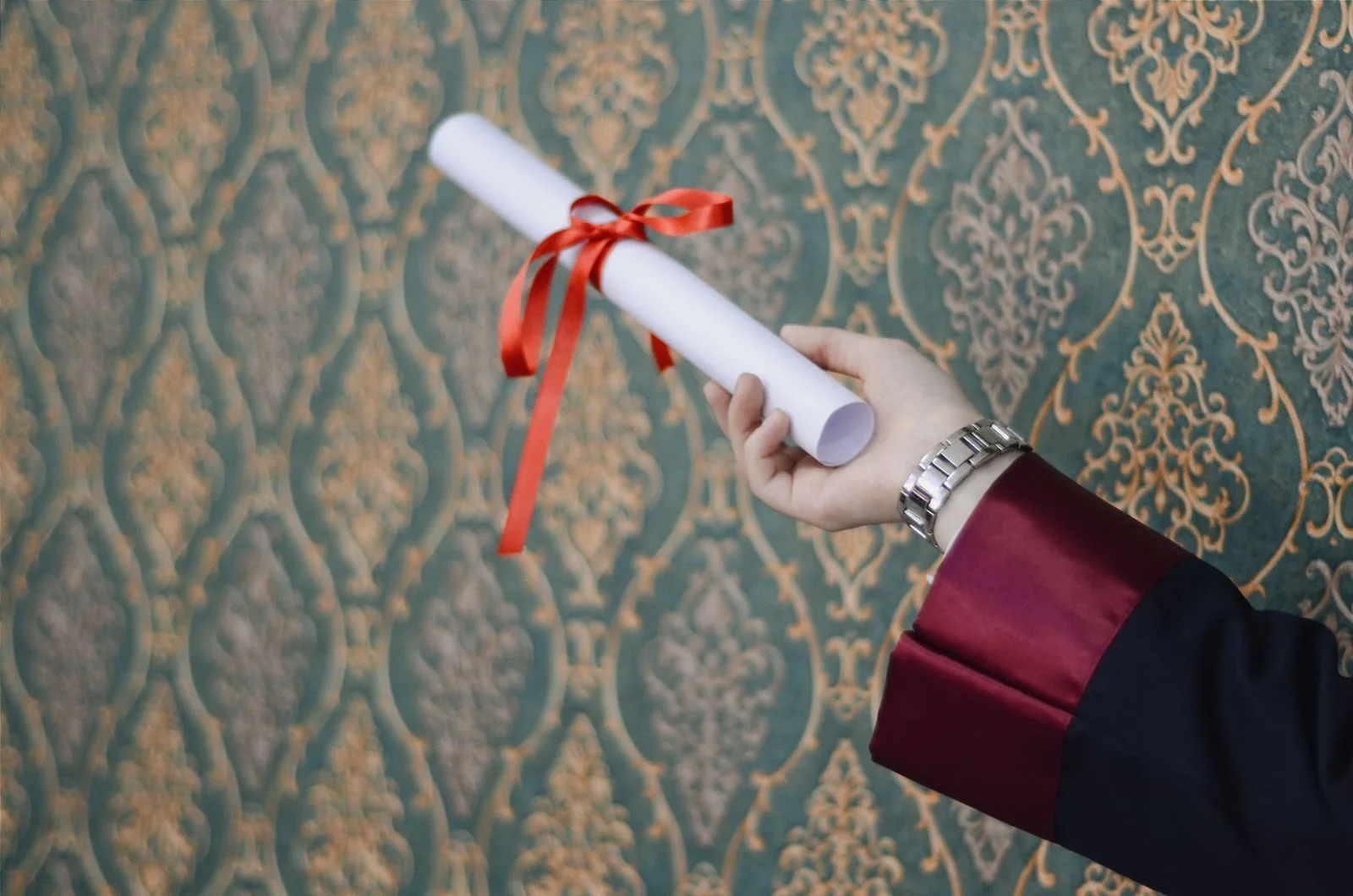 Mano sosteniendo un diploma con lazo rojo, símbolo de un título conseguido