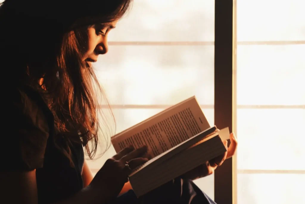 Persona leyendo un libro junto a una ventana, ambiente cálido