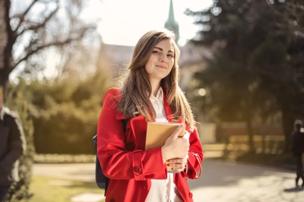 Estudiante universitaria sonriendo con un libro al aire libre
